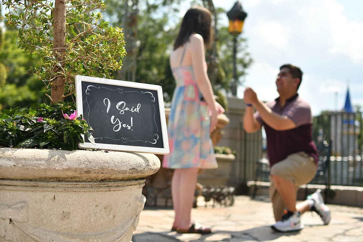 Jesús proposing to Katie with a sign reading "I said yes!" in focus.